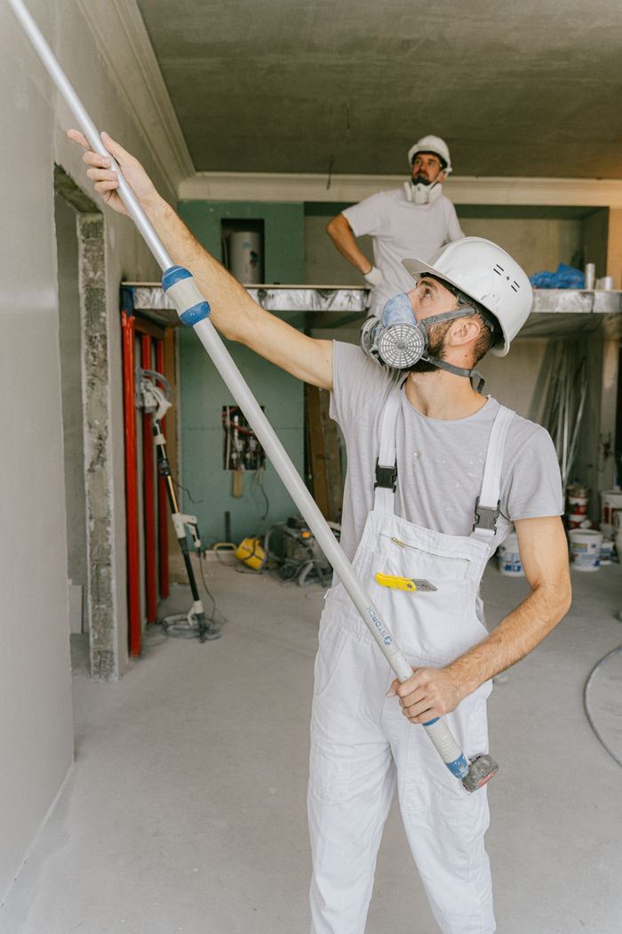 services-04 Two construction workers in safety gear are interior renovating, using a paint roller.