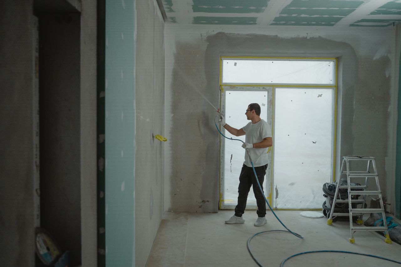 who-we-are A man sprays paint on a wall while renovating an indoor room with professional equipment.